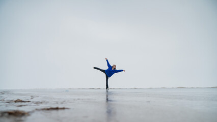 Caucasian woman in a blue sweater is skating on a frozen lake. Figure skater performs a swallow. 
