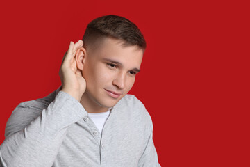 Man showing hand to ear gesture on red background, space for text