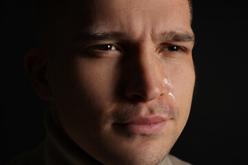 Obraz premium Distressed young man crying on black background, closeup