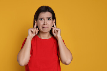 Woman showing hand to ear gesture on orange background, space for text