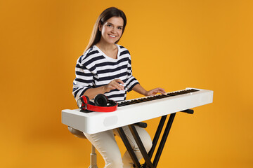 Smiling woman playing synthesizer on orange background