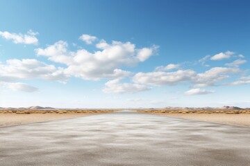 Desert landscape showing a long road stretching towards the horizon under a clear blue sky with clouds