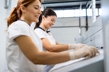 Female laundry workers preparing linen and bedsheets for ironing in dry cleaning service.