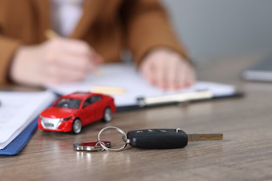 Car key, model and woman signing purchase agreement at wooden table, selective focus. Buying auto