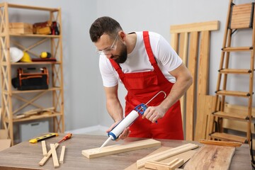 Worker with caulking gun glueing wooden plank indoors