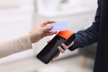 Woman paying with credit card via terminal against blurred background, closeup