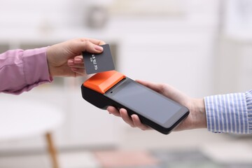 Woman paying with credit card via terminal against blurred background, closeup