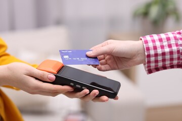 Woman paying with credit card via terminal against blurred background, closeup