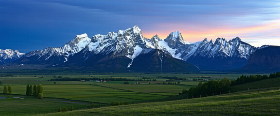 Obraz premium Towering snow-capped peaks glowing in the amber light of sunset, with rolling green valleys below an