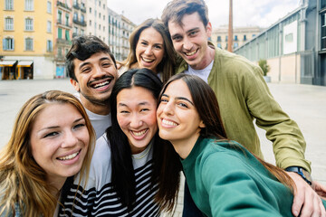 Young group of happy millennial generation people taking selfie portrait outdoors. Diverse friends enjoying day off at city street. Youth community and friendship concept