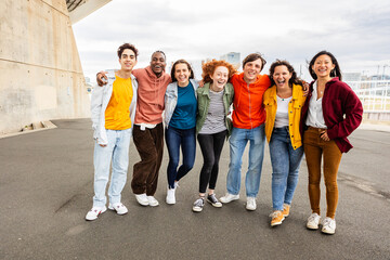 Happy young group of teen friends hugging each other smiling at camera outside. Youth community concept