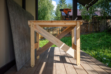 homemade wooden table on which a cordless screwdriver stands against the background of greenery and country landscape