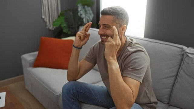 Young man crossing fingers then celebrating in living room showcasing excitement and hopefulness at home indoors.