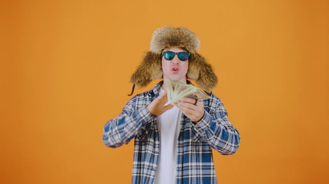 A man in sunglasses and a warm ushanka hat joyfully throws dollar bills while saying "I'm rich " The scene captures his exuberance and wealth in a lively and engaging setting