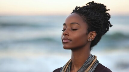 African female adult meditating peacefully by ocean at sunset