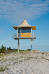 Elevated yellow lifeguard hut on a sandy beach with blue sky.