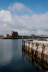 Wooden pier and calm waterfront with industrial buildings under clouds & historic red brick Harts Mill Flour Shed in distance