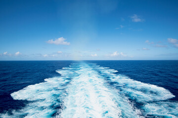 Ocean wake trail under a bright blue sky with scattered clouds