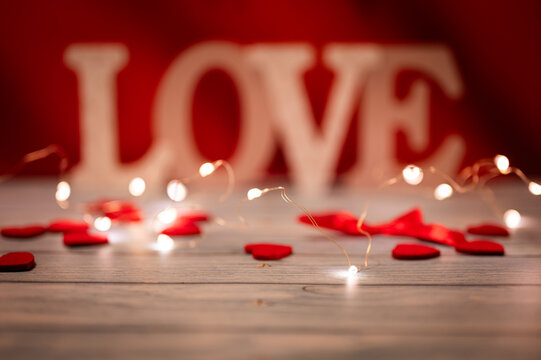 Love text big letters and red hearts on a red wooden background with lighting