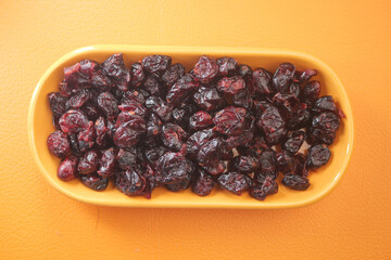 A bowl filled with dried cranberries placed on a vibrant orange background