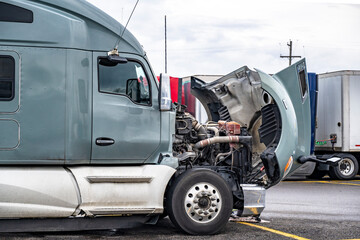 Broken gray big rig semi truck with open hood standing on the truck stop parking lot waiting for qualified repair