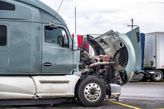 Broken gray big rig semi truck with open hood standing on the truck stop parking lot waiting for qualified repair