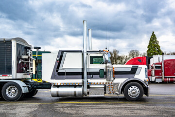 Classic white low cab profile big rig semi truck with high exhaust pipes and bulk semi trailer standing on the truck stop parking lot