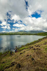 Peaceful lakeside scene. Calm water reflects the cloudy sky and distant mountain range.