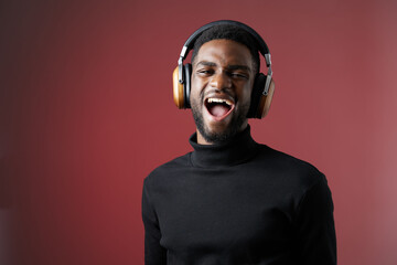 Young Black man joyfully wearing headphones, expressing happiness, in a modern and stylish setting with a warm red background, perfect for music and lifestyle themes