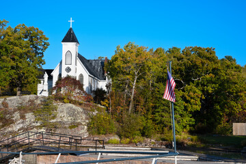 Rockport Ontario Canada St. Brendan&rsquo;s Church. The church is perched on a rocky hill surrounded by lush green trees. The clear blue sky adds to the serene and picturesque setting