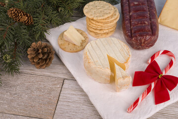 Cheese, charcuterie and crackers on a white ceramic plate. White wooden plank in background. Christmas holiday theme.