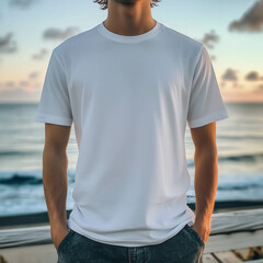 A person wearing a plain white t-shirt, standing on a boardwalk overlooking the ocean