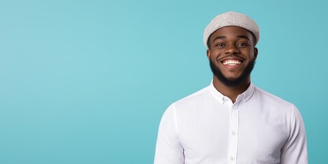 Obraz premium A joyful young man with a charming smile and a fashionable hat stands in front of a vibrant blue background, capturing the essence of enthusiasm and confidence in modern fashion.