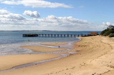 Beach with a jetty pier under a blue sky with fluffy clouds at Cowes on Phillip Island in Victoria,...