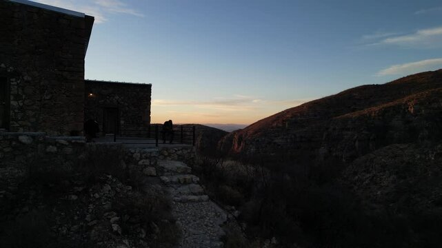 Fotograf&oacute; con un teleobjetivo tomando una fotograf&iacute;a en el atardecer sobre una monta&ntilde;a y un edificio de piedra