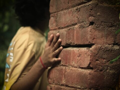 A cinematic shot primarily focused on the hand of the boy on the red brick wall in a dense forest aravali hill
