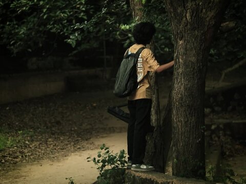 a wide shot of a boy standing near a tree looking at something at aravali hills, back shot

