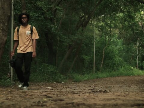 An Indian boy wearing a cream colored t shirt walking in a dense evergreen forest near the aravali hills, cinematic shot, wide

