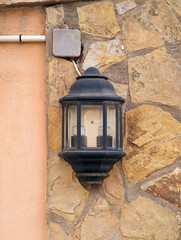 Close-up of black metal unlit rustic wall lantern  against natural stone textured facade by day,...