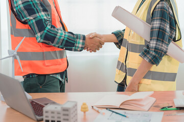 Contractor and businessman holding hands in construction office with house plans on table, concept: cooperation and trust are the keys to building a successful project. Close-up pictures