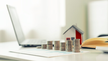 Stack of coins with a small house on the background - concept illustration of real estate investment, house purchase or maintenance: small house model money saving concept