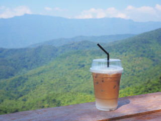 take away glass of capuccino coffee over green mountain background.