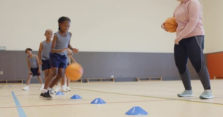 Dribbling basketball around cones, children practicing in school gym with coach