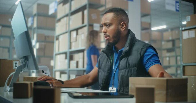 African American post office employee scans cardboard parcel using barcode scanner, works on computer. Sorting center workers carrying boxes for delivery to clients. Online E-commerce shop warehouse.