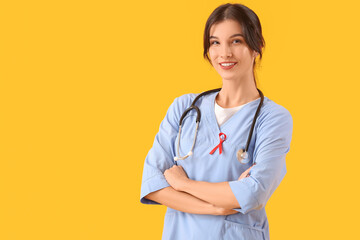 Young female doctor with red ribbon on yellow background. World AIDS day concept