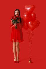 Beautiful young woman with kiss marks on her face holding bouquet of roses and heart shaped air balloons on red background
