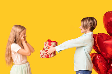 Little boy greeting girl with gift on yellow background. Valentine's Day celebration