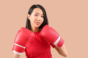 Beautiful young Asian woman in boxing gloves on beige background. Women history month