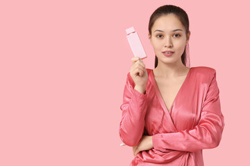 Beautiful young Asian woman with bottle of perfume on pink background