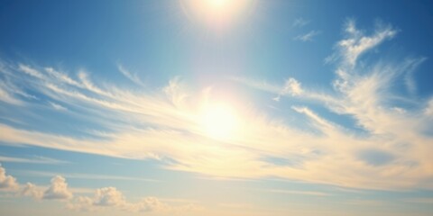 Obraz premium A bright sun shines through feathery clouds, casting a warm glow on the blue sky